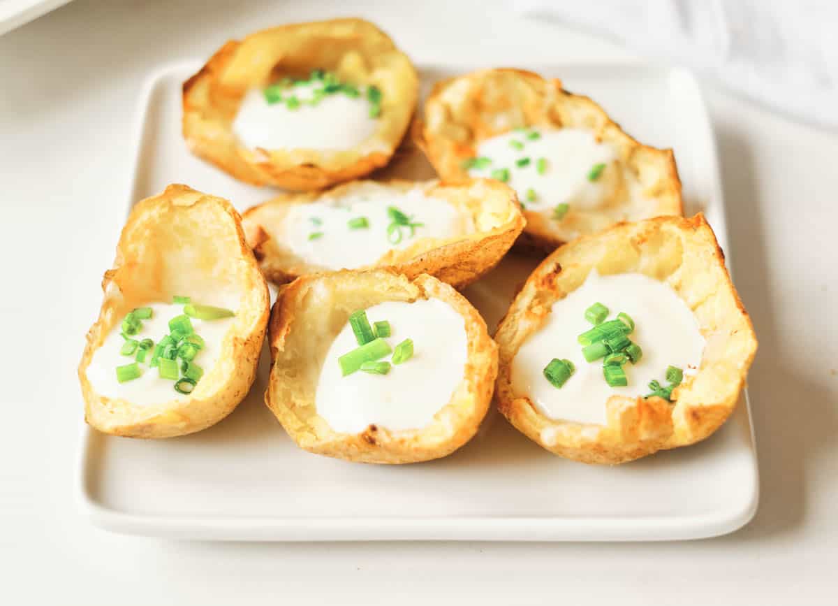 air fryer potato skins on a white square plate filled with cheese, sour cream, and chives