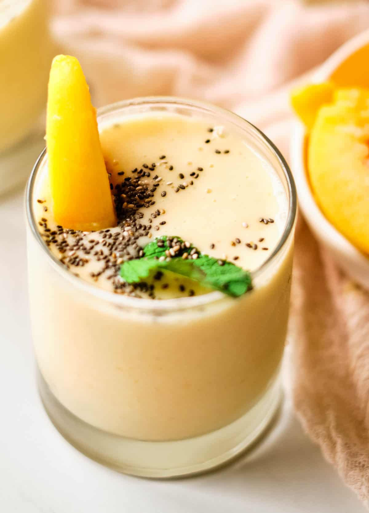 overhead of peach and banana smoothie topped with mint, peach slice, and chia seeds