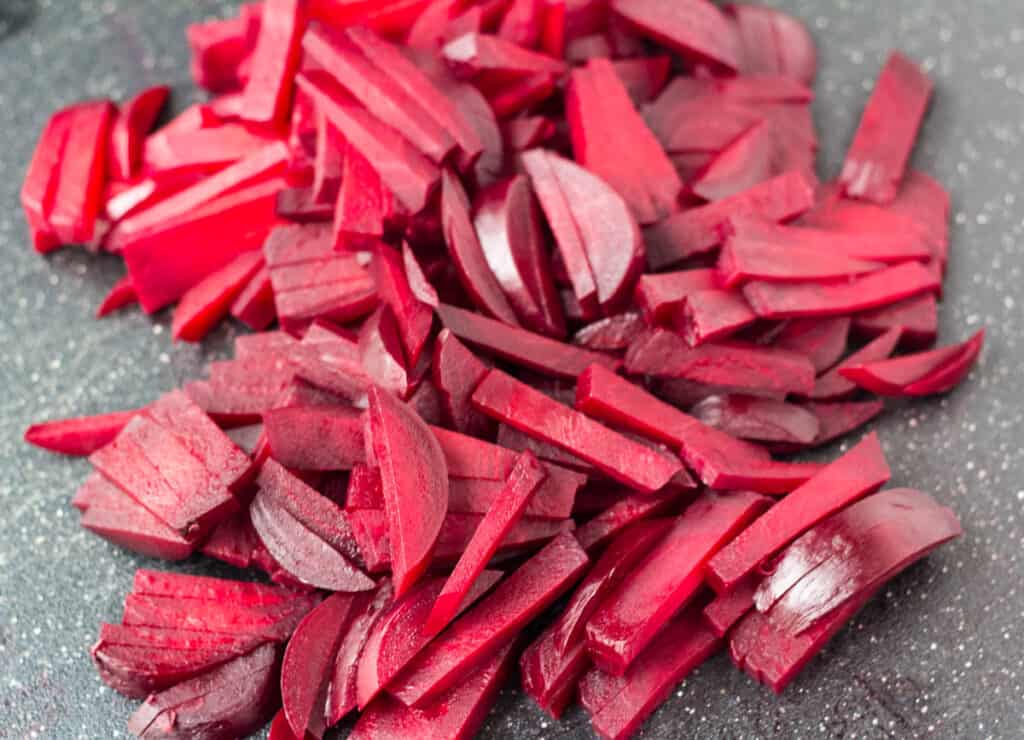 cooked beetroot sliced into strips on black cutting board