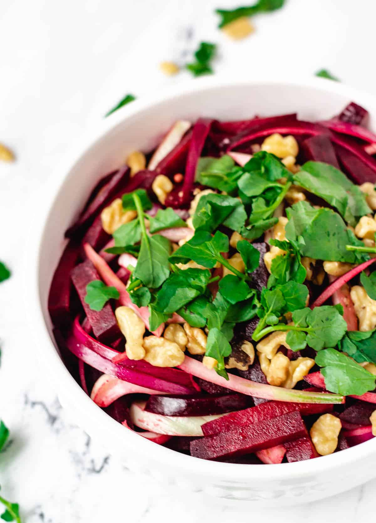 close up of beetroot salad in white bowl topped with watercress and walnuts
