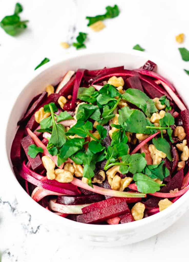 beetroot salad in white serving bowl topped with watercress and walnuts