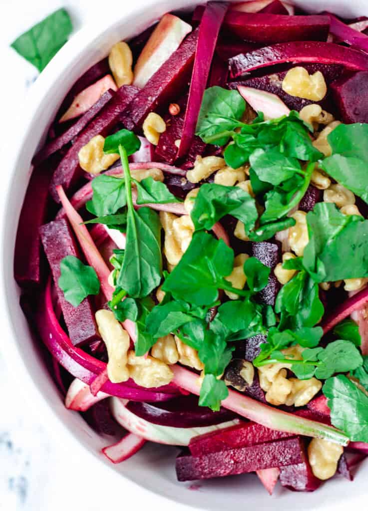 close up overhead of beetroot salad in serving bowl topped with walnuts and watercress