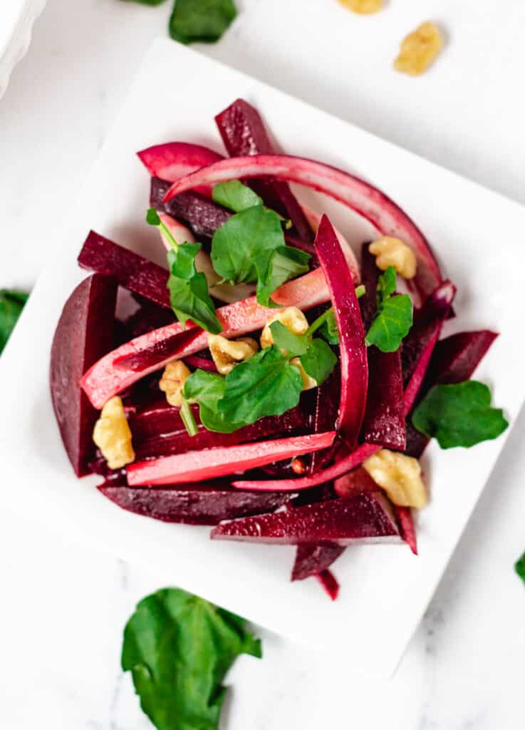 small serving of beet salad on white plate topped with watercress and walnuts