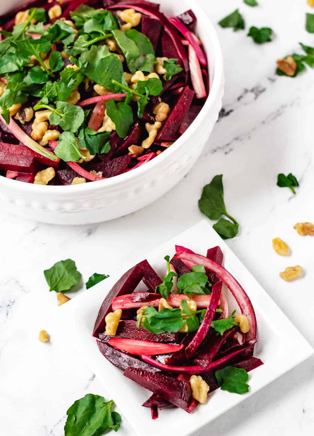 beetroot salad in white serving bowl next to small serving size of salad on white dish