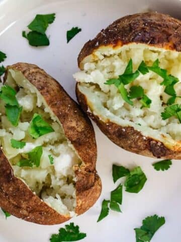 Two baked potatoes on a white plate.