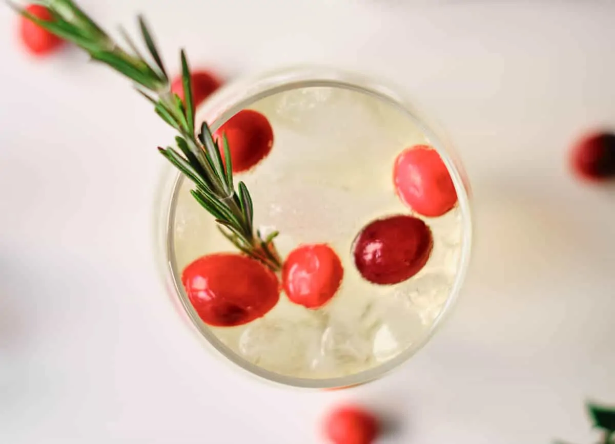 Orange mocktail garnished with cranberries and rosemary.
