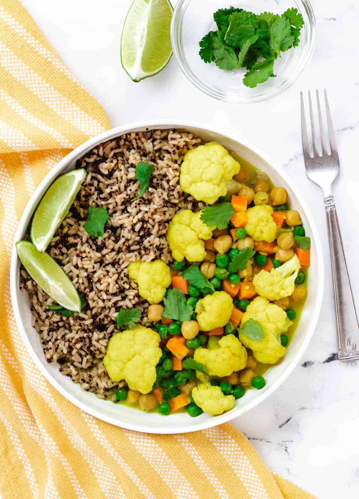 Cauliflower curry in white bowl served with rice and lime wedges.