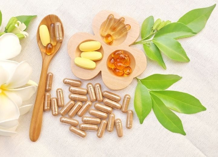 variety of vitamins on cloth with leaves, flower on wood spoon, and wood tray