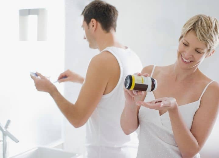 man and woman taking vitamins in their bathroom