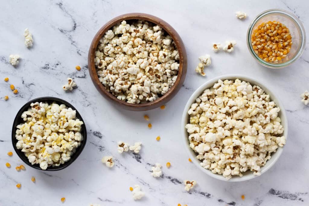 three bowls of popcorn and jar filled with popcorn kernels