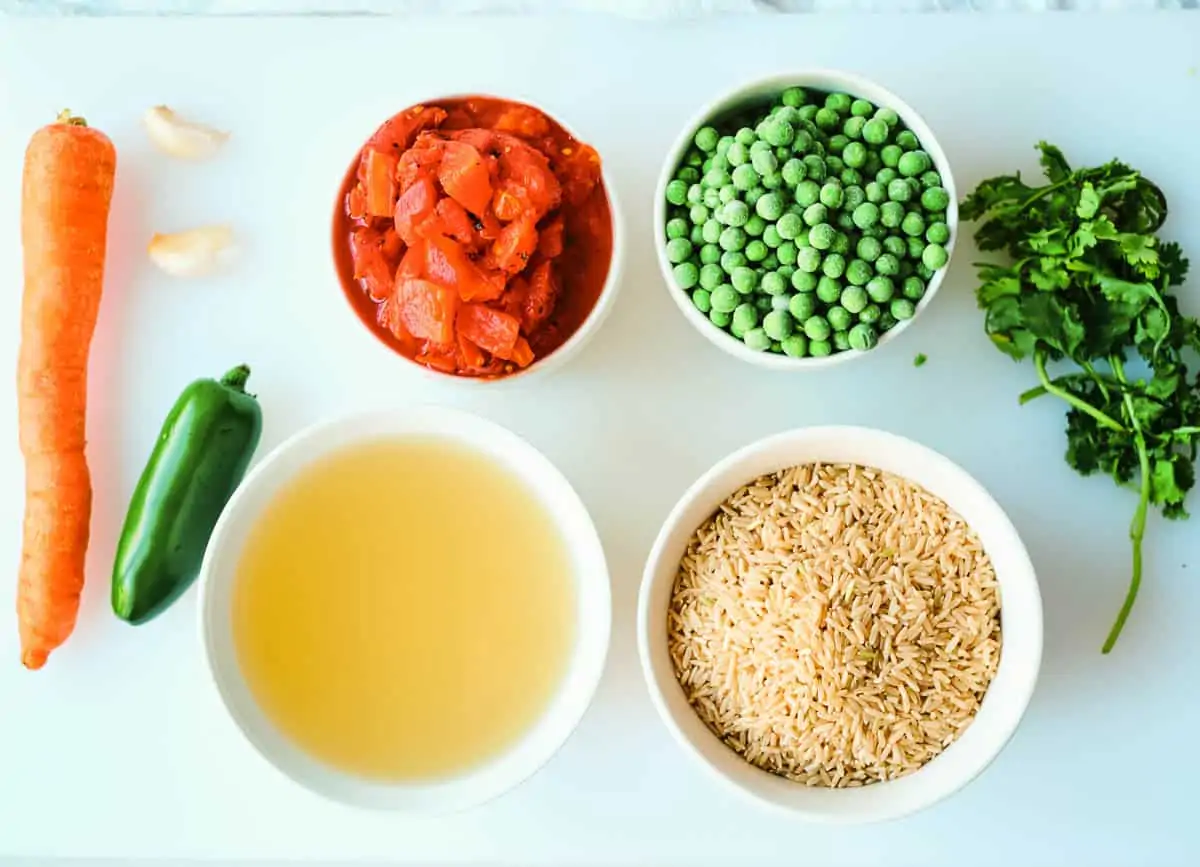 ingredients for arroz rojo on cutting board: 1 carrot, 1 jalapeño pepper, two cloves of garlic, vegetable broth, fire roasted tomatoes, frozen peas, rice, and cilantro