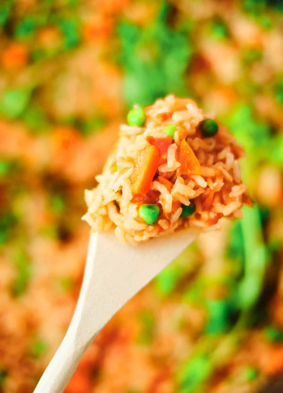 close up of red rice on wooden spoon with peas and carrots