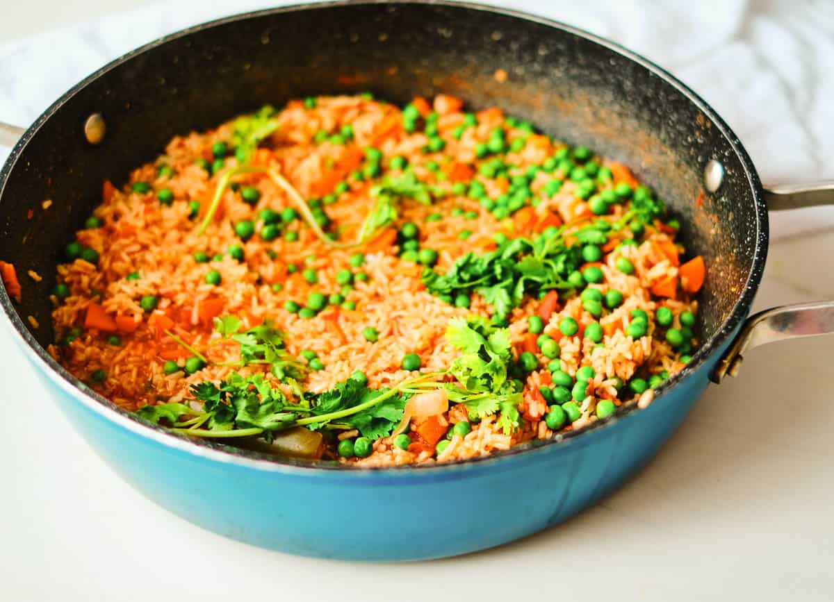 Mexican red rice in blue pot topped with peas and cilantro
