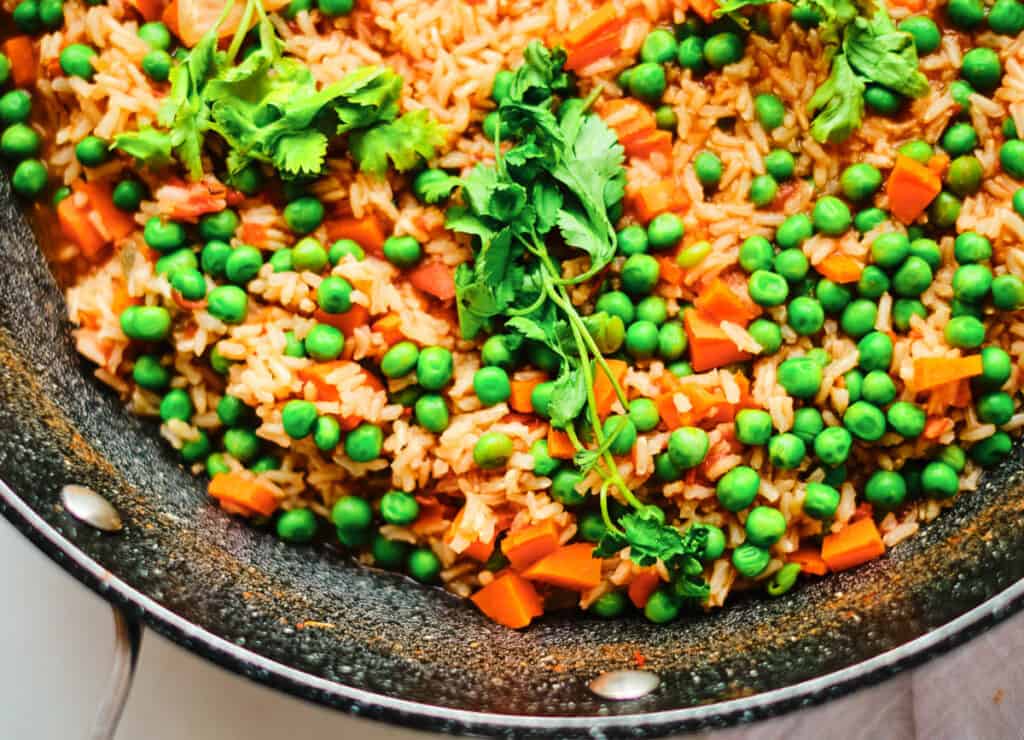 overhead of Mexican red rice in pot topped with peas and carrots, and cilantro 