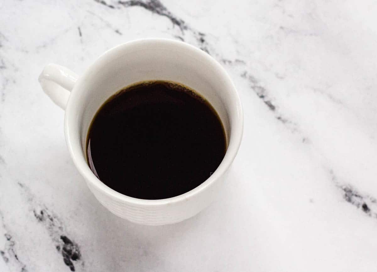 Small white mug filled half with black coffee.