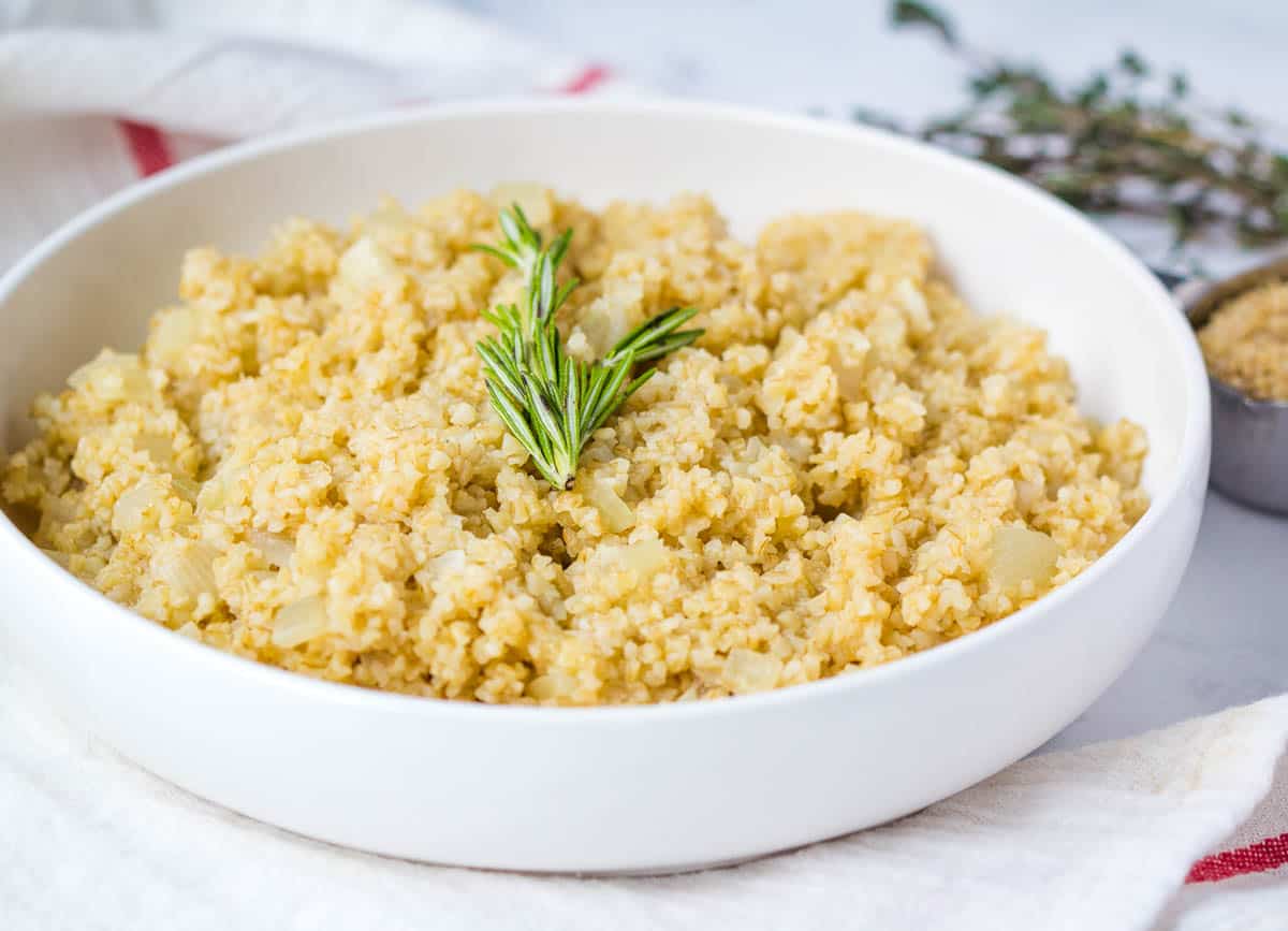 Cracked wheat with onions in white bowl topped with rosemary.