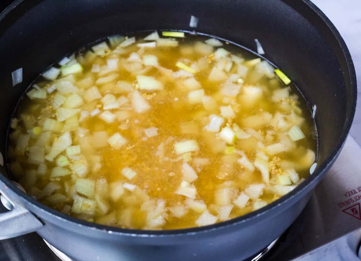 Onions, broth, and bulgur simmering in saucepan.