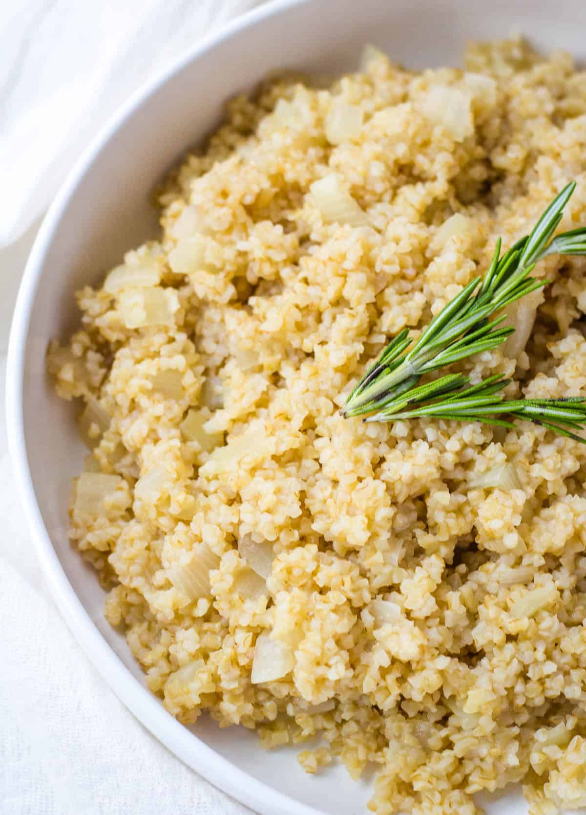 Close up of bulgur pilaf with onions topped with rosemary.