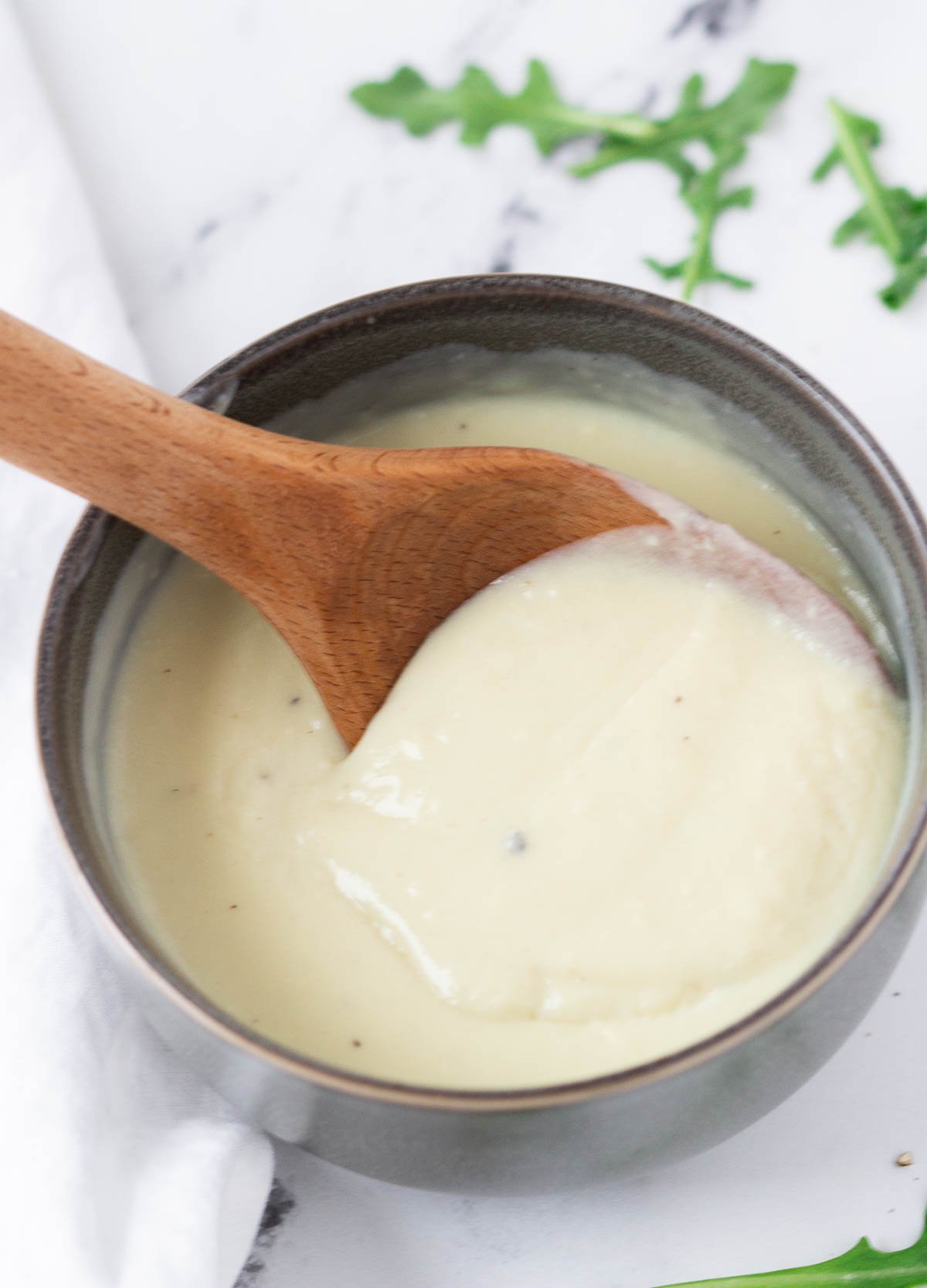 close up of wooden spoon scooping a spoonful of vegan béchamel sauce from gray bowl