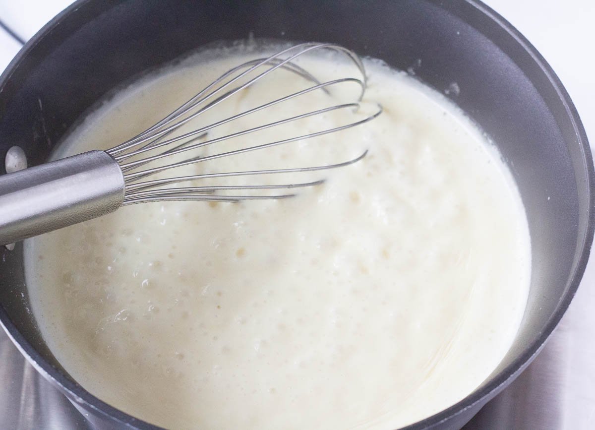 Bubbling white sauce in pot with whisk.
