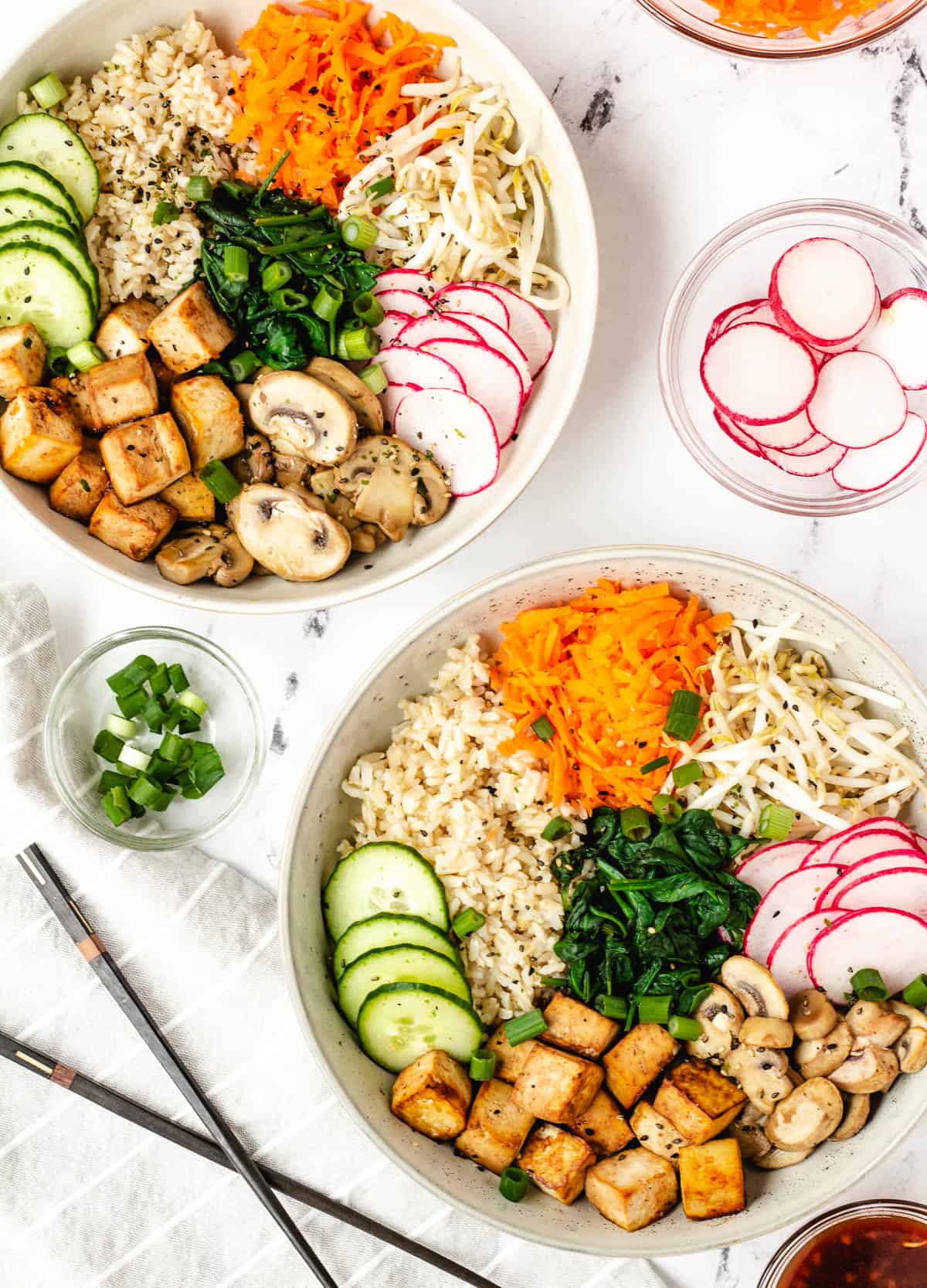 Two bowls of vegan bibimbap with chopsticks and bowl of radishes.