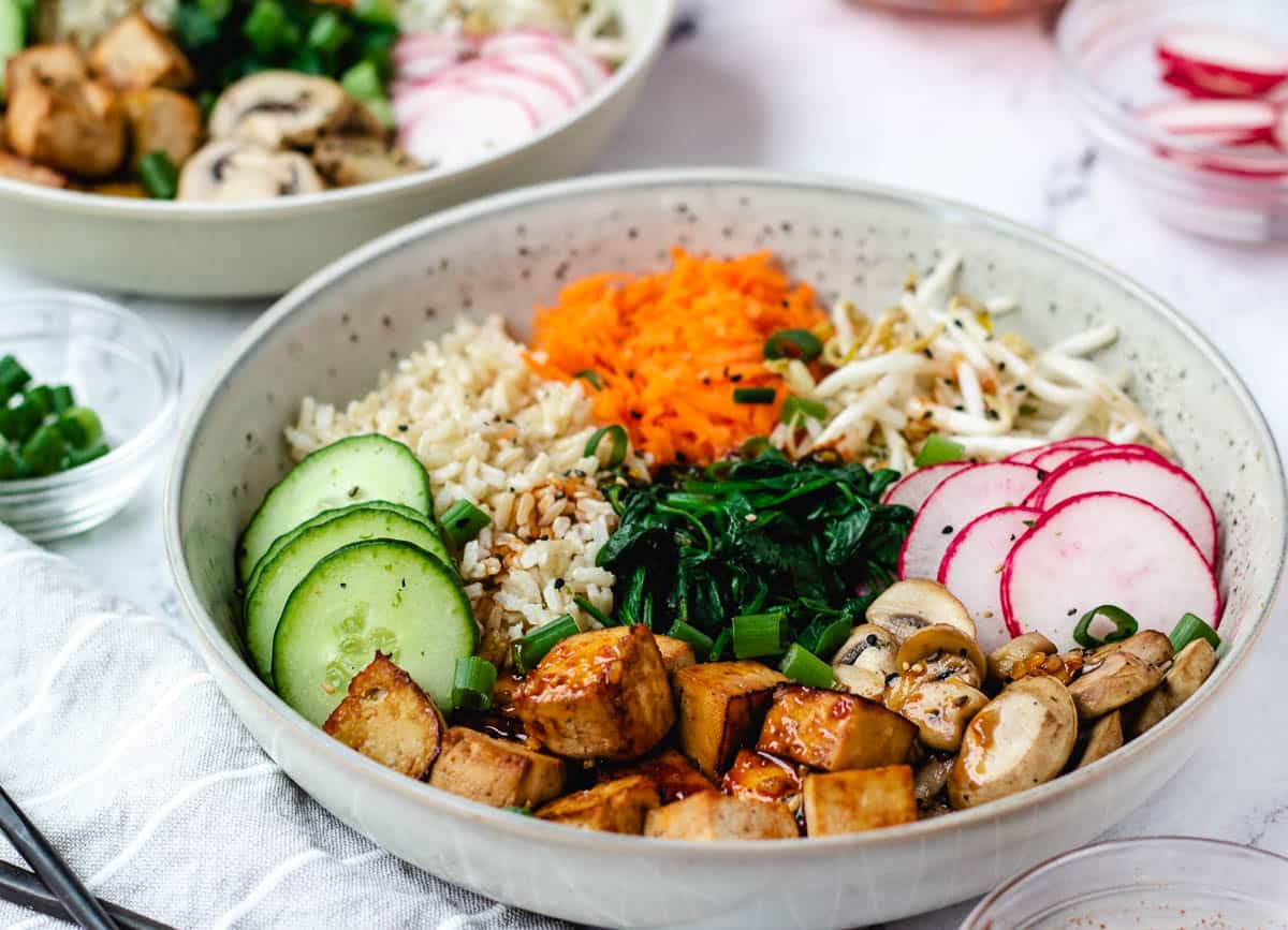 Close up of vegan bibimbap in gray bowl with mixed vegetables and baked tofu.