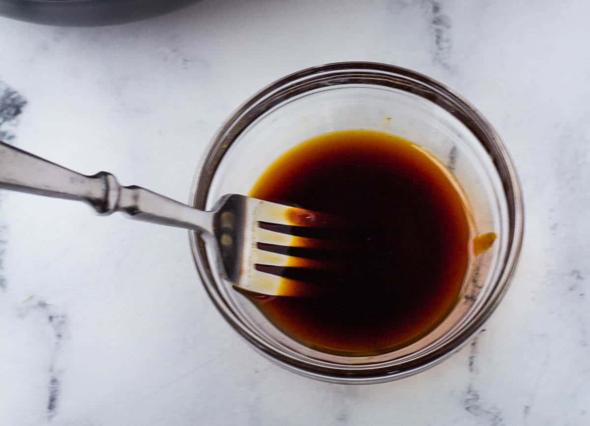 Fork whisking marinade in small glass bowl. 