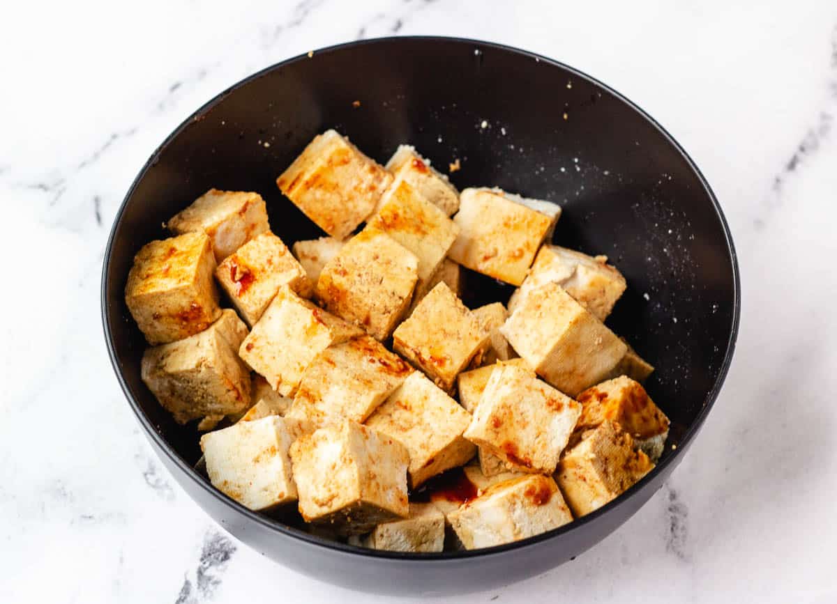 Tofu covered in marinade in black bowl. 