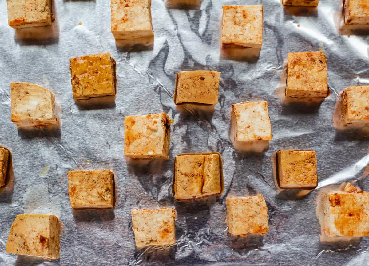 Marinated tofu cubes on aluminum lined baking sheet.