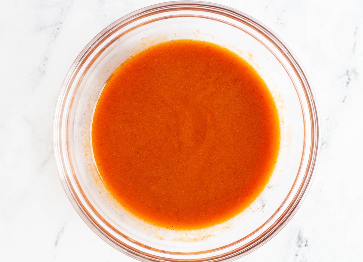 Vegan buffalo sauce whisked together in a glass bowl.
