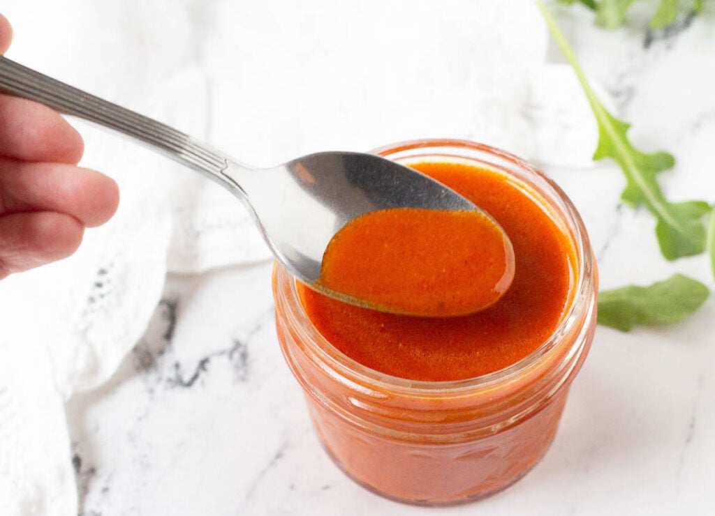 hand scooping buffalo sauce on spoon a spoon from glass jar