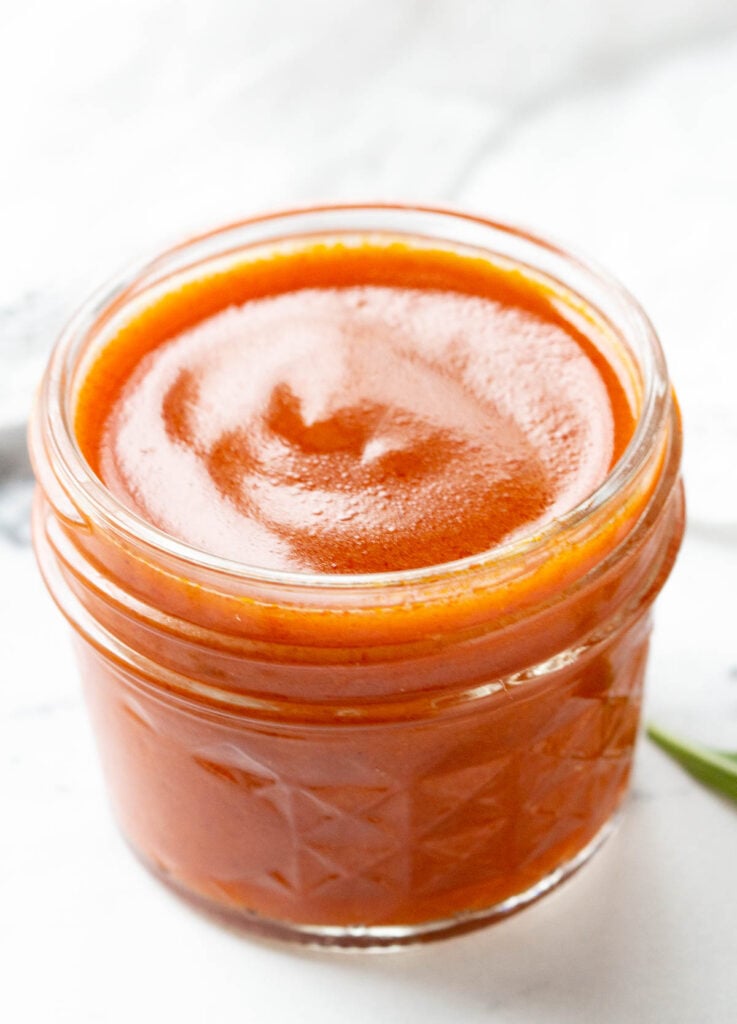 close up of orange buffalo sauce in glass mason jar 