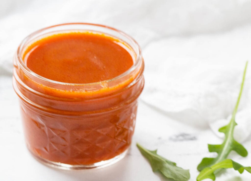 buffalo sauce in jar off to the side beside arugula and white napkin