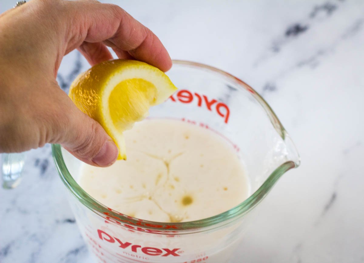 hand squeezing lemon juice into pyrex measuring cup filled with soy milk