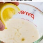 hand squeezing lemon into milk in a measuring cup