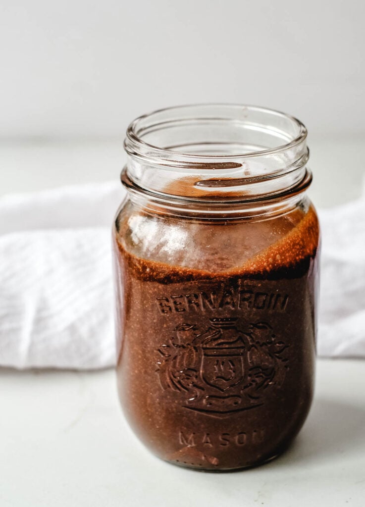 mason jar filled with chocolate sauce on sitting on white counter top with white dish cloth in the background