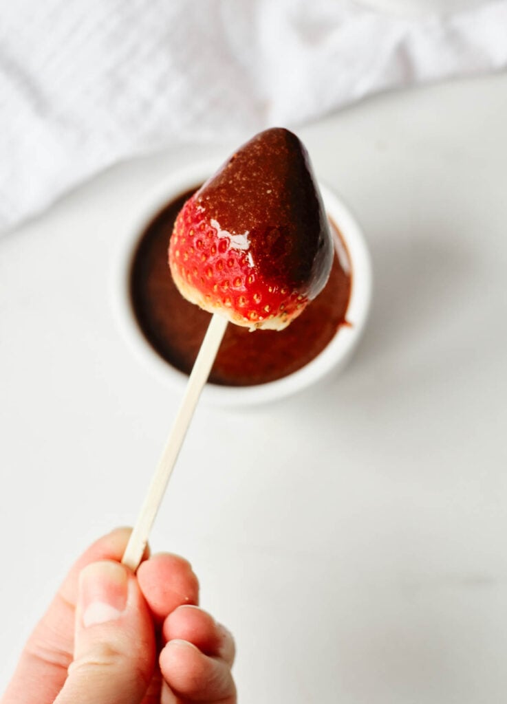 overhead of hand holding strawberry on stick dipped in chocolate sauce