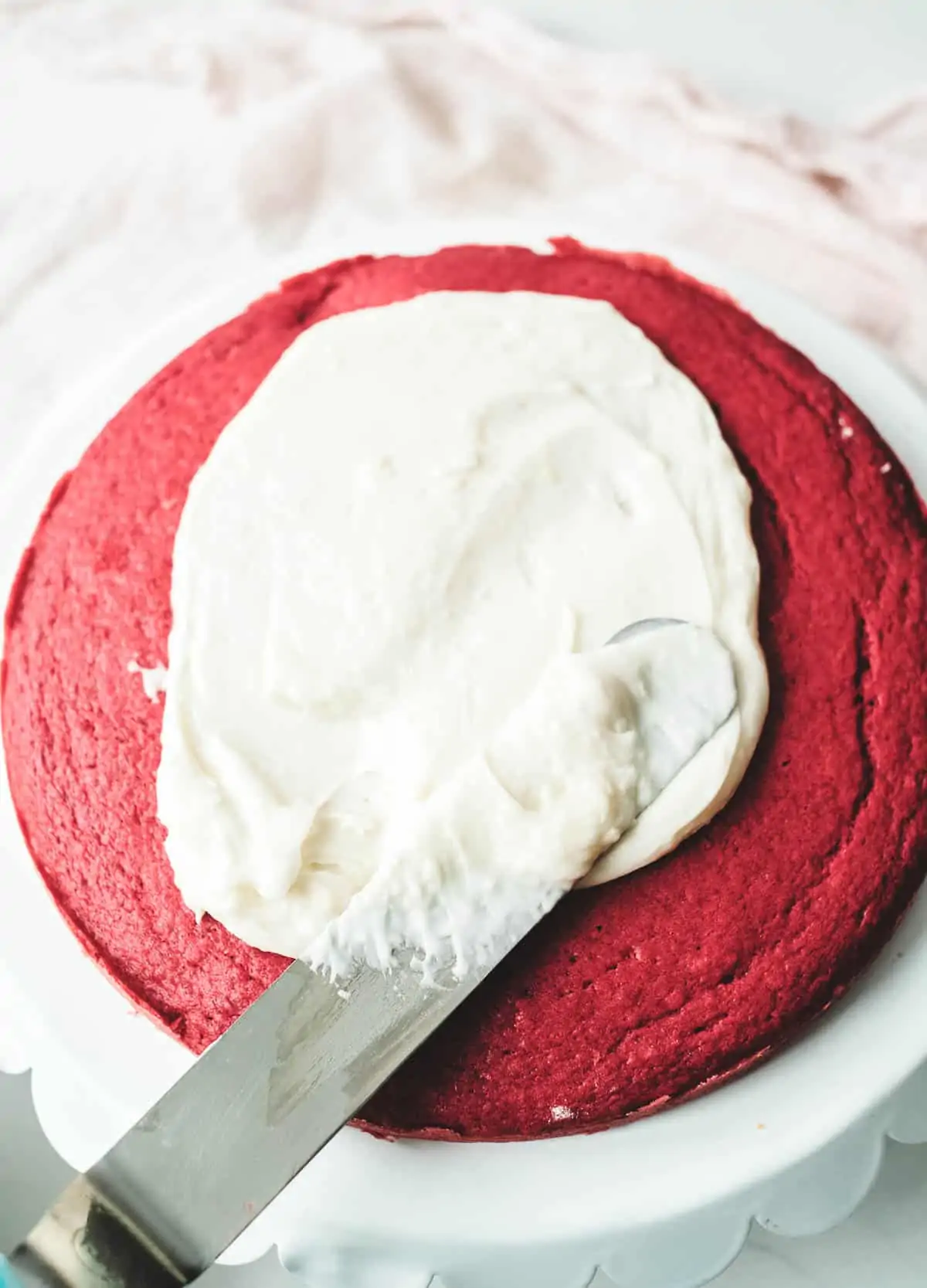 Cream cheese frosting on top of a layer of red cake.
