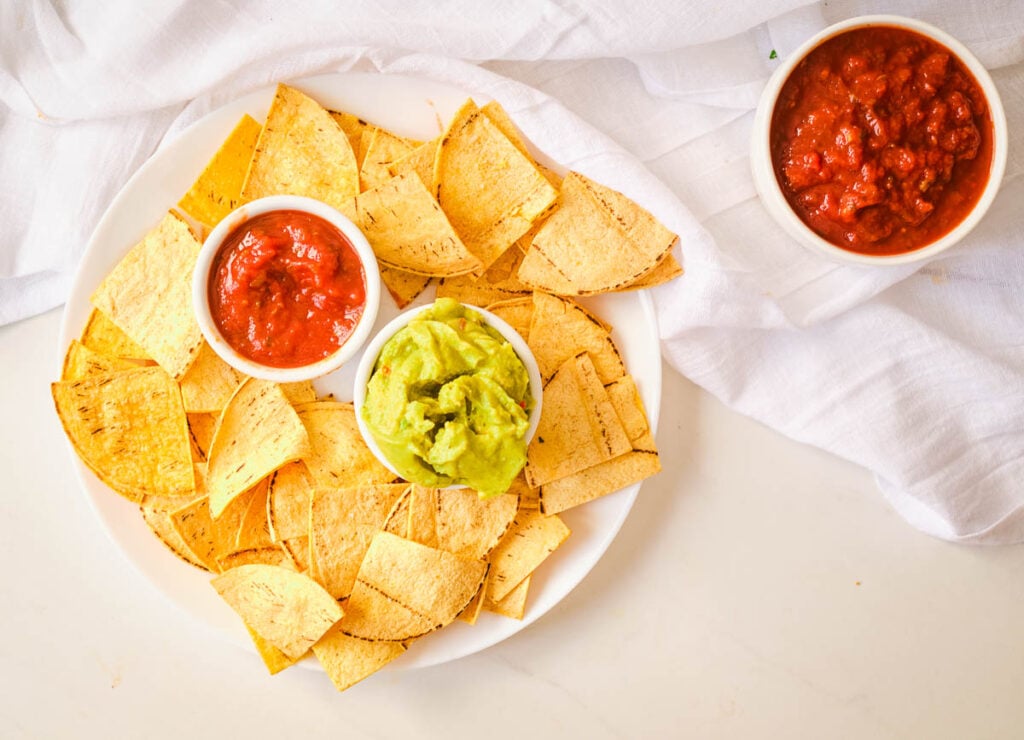 Plate of tortilla chips with small bowls of salsa and guacamole.
