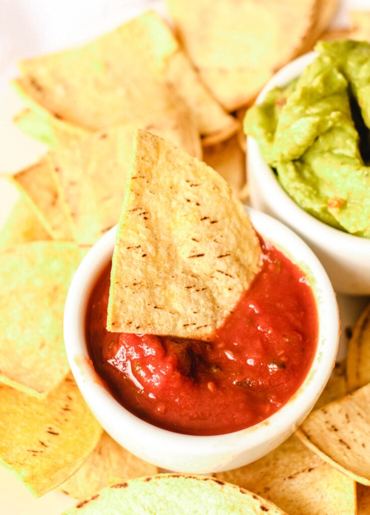 Chip in small bowl of salsa, surrounded by other chips, and a side of guacamole.
