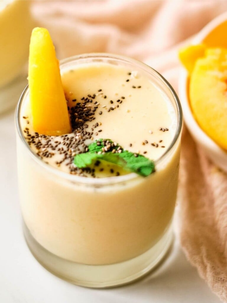 banana peach smoothie in a highball glass topped with chia seeds, mint, and a peach slice