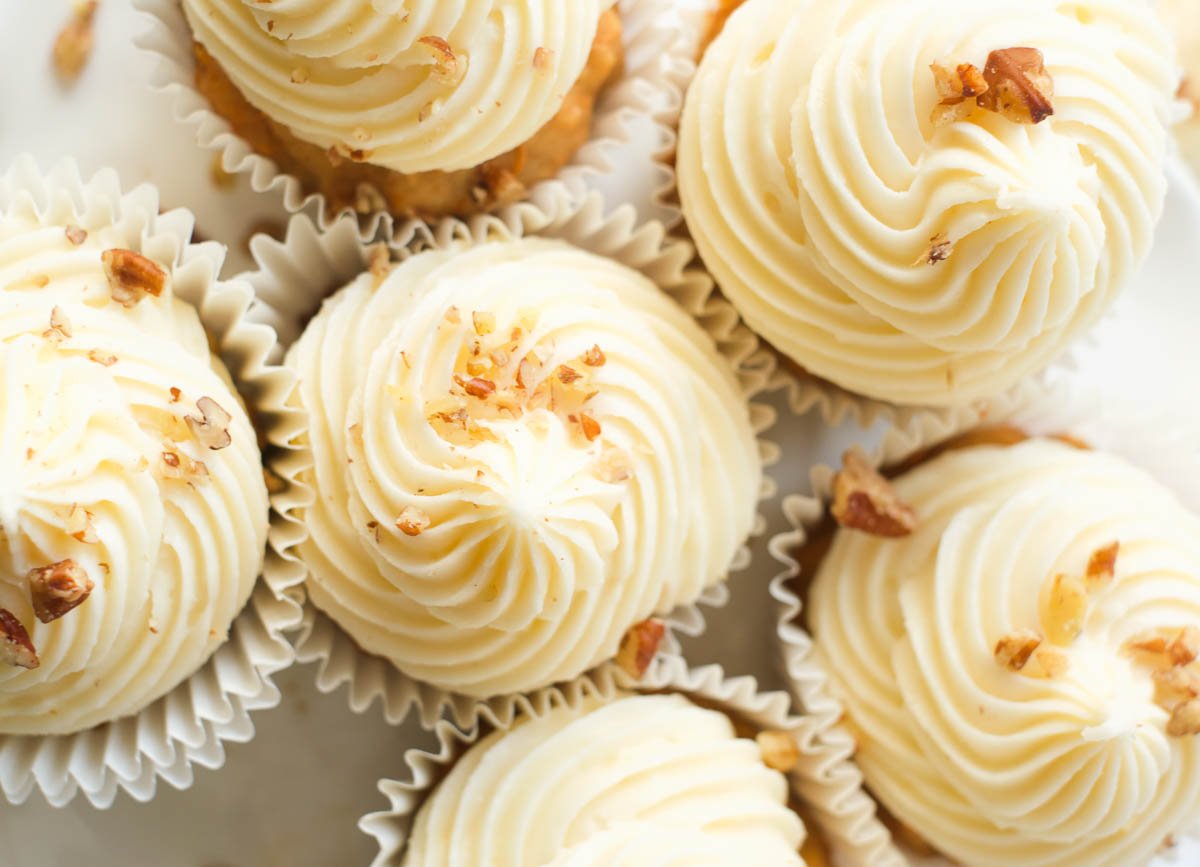 Overhead of carrot cake cupcakes topped with cream cheese frosting and chopped walnuts.
