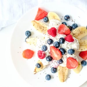 healthy banana split with fresh berries and yogurt on white plate