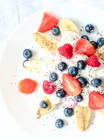 healthy banana split with fresh berries and yogurt on white plate