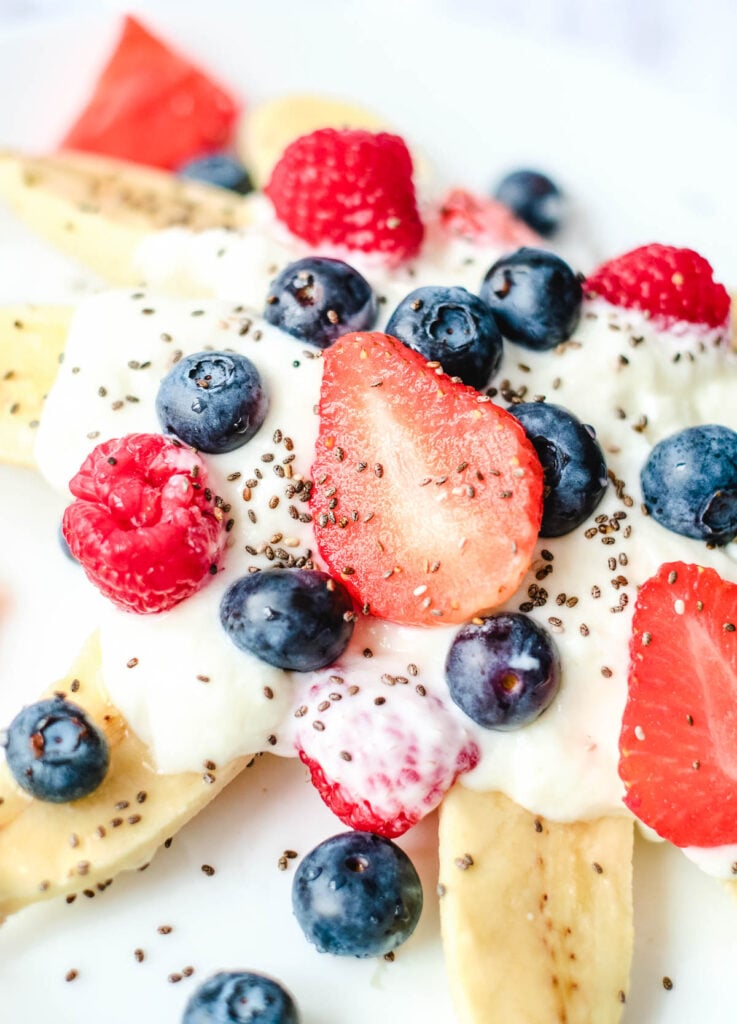 banana slices, topped with yogurt, raspberries, strawberries, and blueberries, with chia seed sprinkles