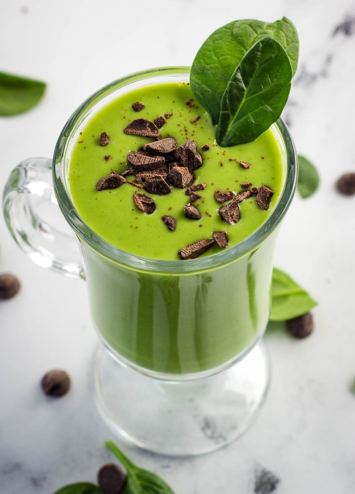 Green vegan shamrock shake in glass topped with chocolate shavings and spinach leaves.