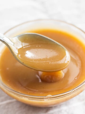 caramel sauce on spoon over bowl filled with caramel sauce