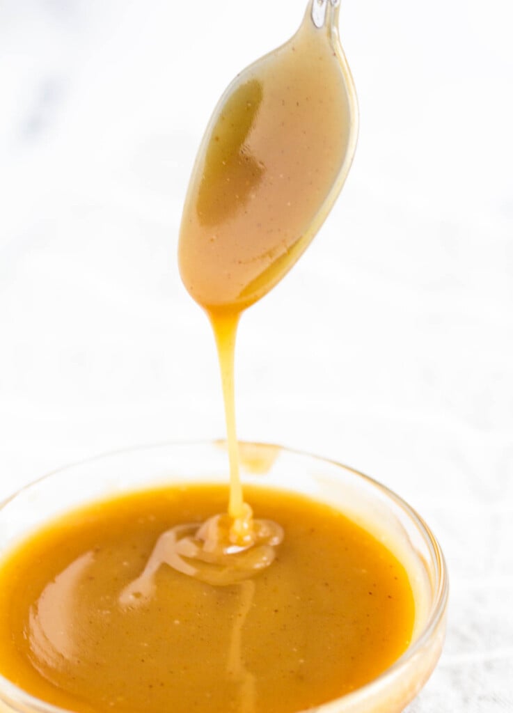 caramel sauce dripping off of spoon into bowl of caramel sauce