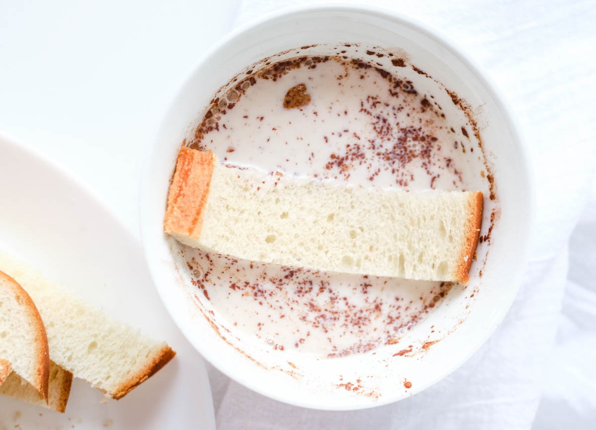 bread strip dipped in bowl of almond milk and cinnamon
