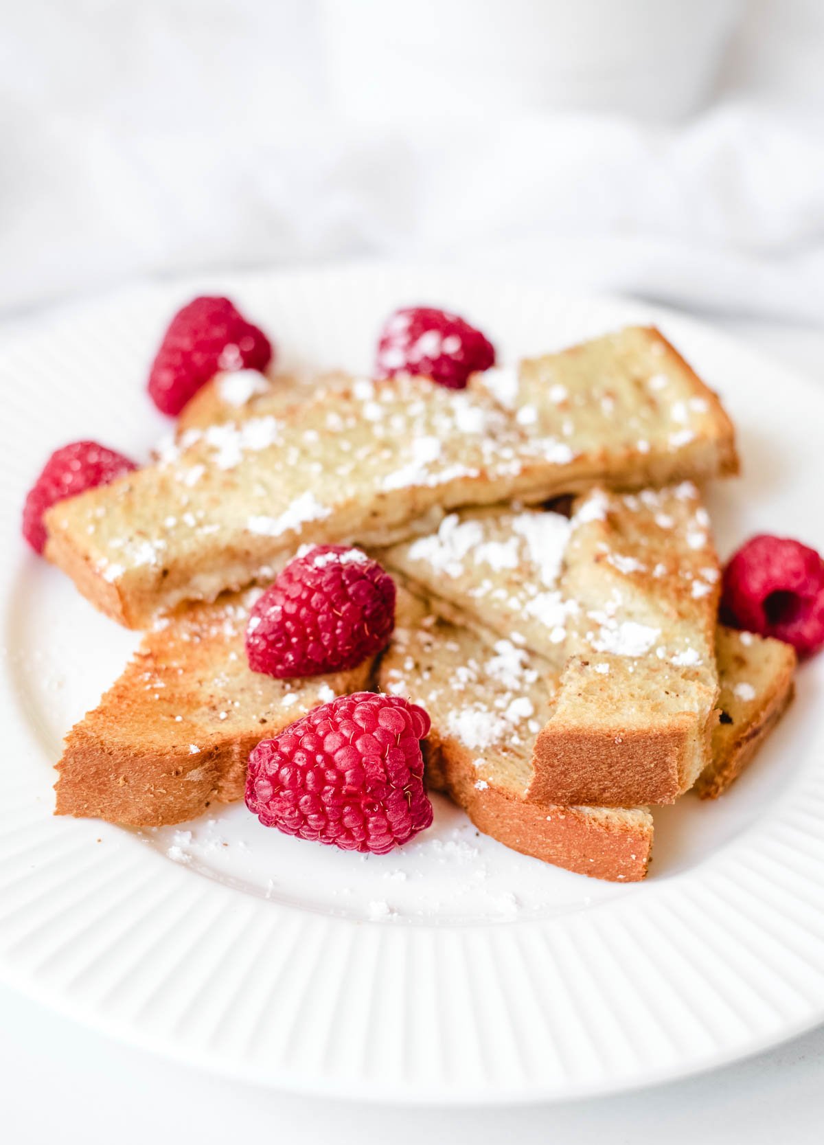 vegan French toast sticks on white plate topped with powdered sugar and fresh raspberries